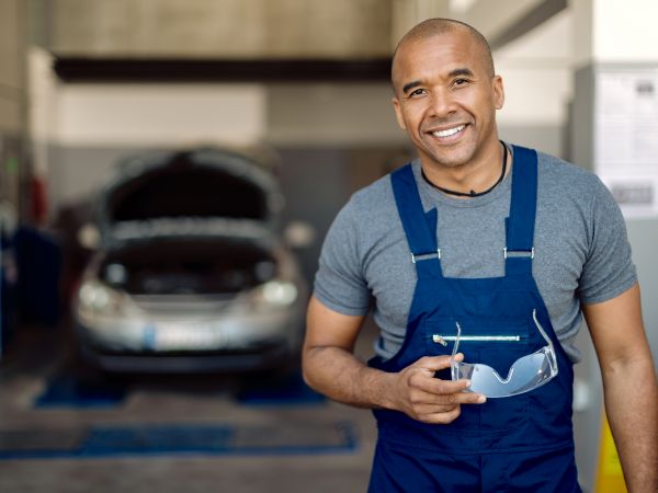 Portrait of happy black mechanic working in auto repair shop and looking at camera.